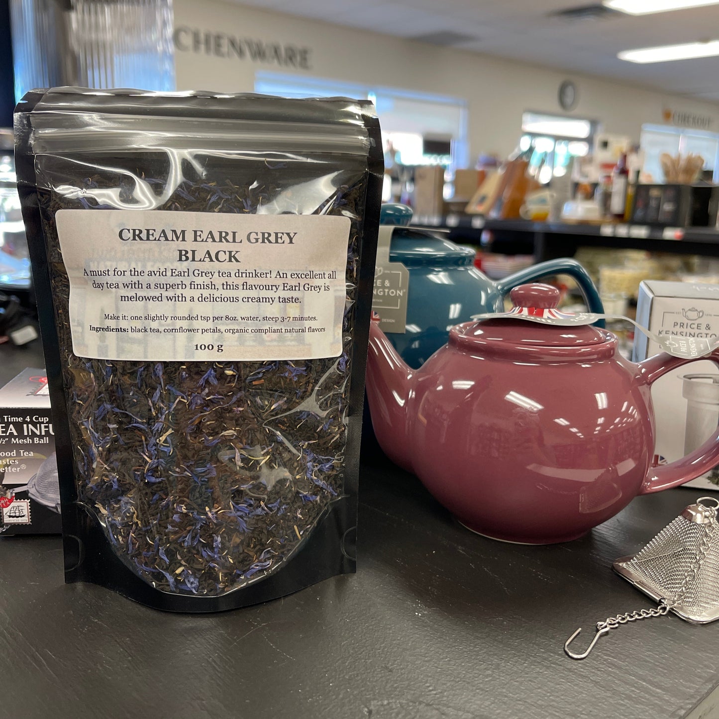 Package of cream earl grey black tea on a table with teapots and a diffuser.