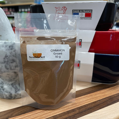 Plastic bag of ground Cinnamon, 50g, sitting on a cutting board.