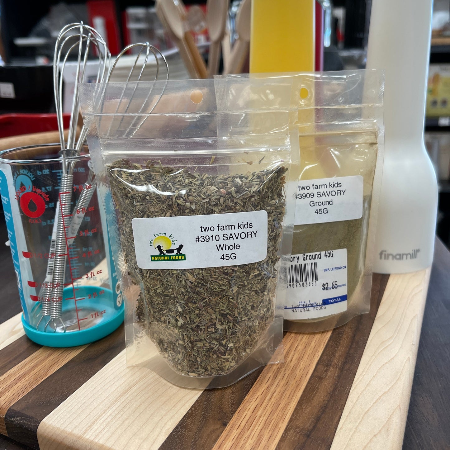 Packaged savory spice, ground and whole, on a wooden cutting board with a blurred background