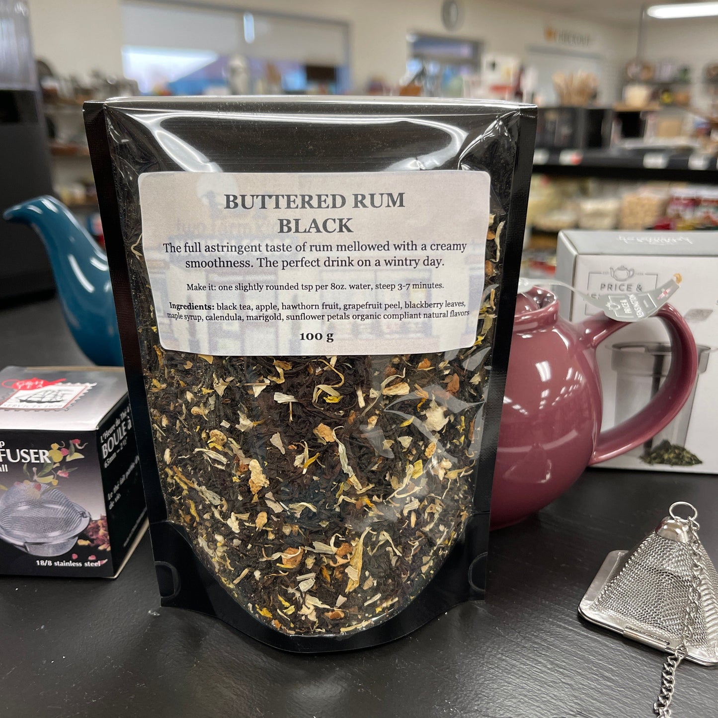 Resealable bag of buttered rum black tea on a table with teapots.