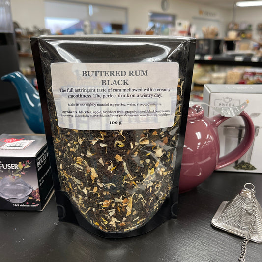 Resealable bag of buttered rum black tea on a table with teapots.
