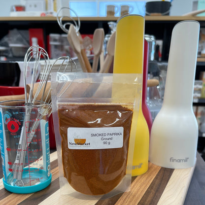 Wooden cutting board with a package of paprika and a measuring cup on a cutting board.