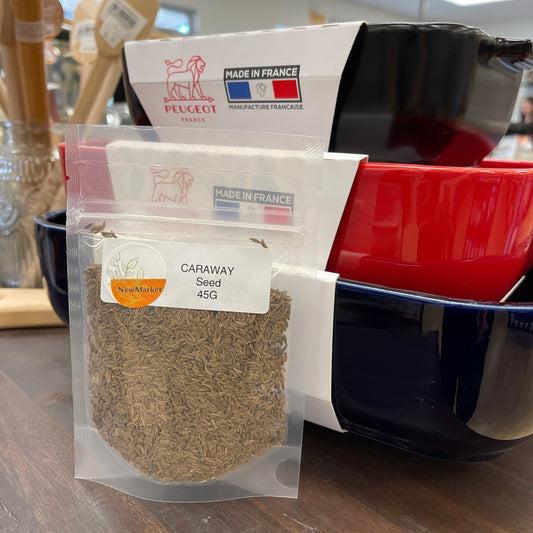 Resealable clear plastic bag of caraway seed on a table with dishes in the background.