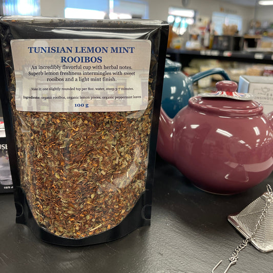 Package of tunisian lemon mint rooibos tea on a table with teapots and tea diffusers.