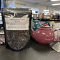 Package of cream earl grey black tea on a table with teapots and a diffuser.