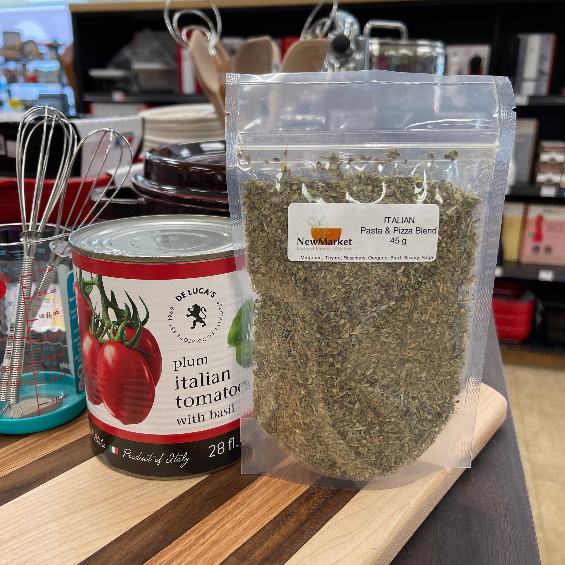 Packaged italian herbs on a kitchen counter with a jar of plum tomatoes and whisk in the background.