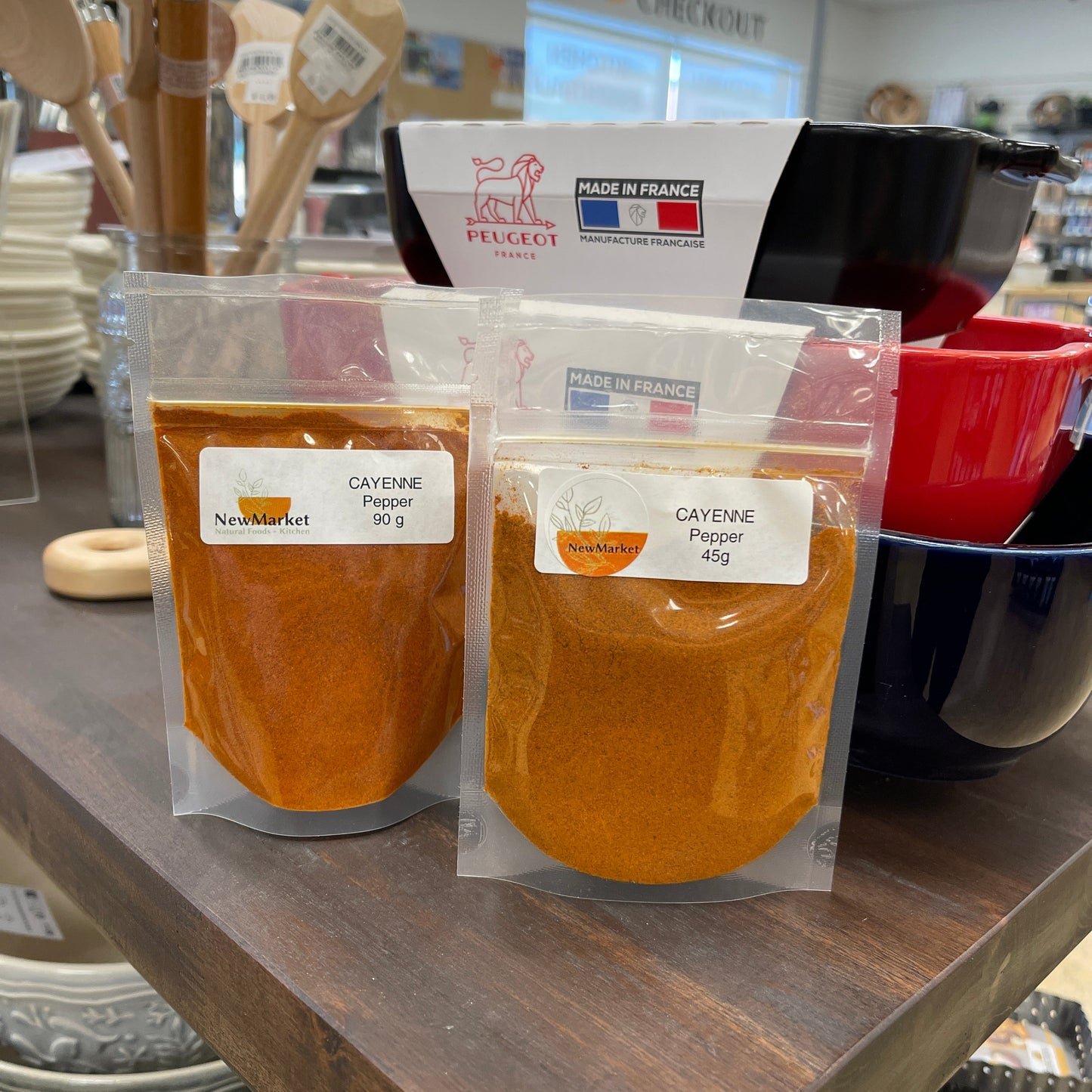 Two packages of cayenne pepper on a table with dishes in the background.