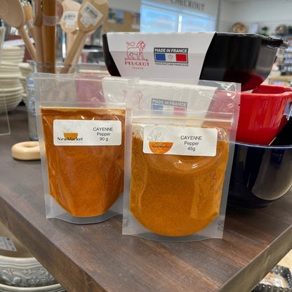 Two packages of cayenne pepper on a table with dishes in the background.