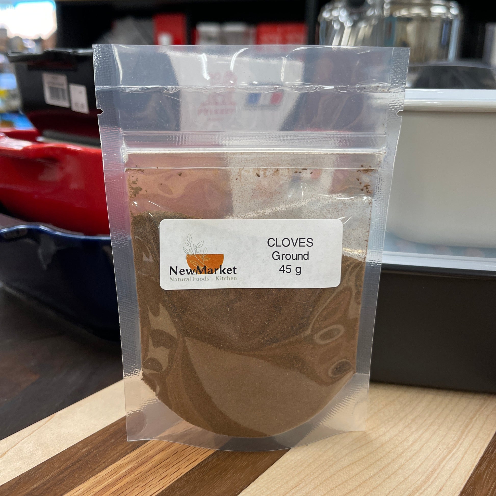 Packaged cloves of ground spice with a NewMarket label on a wooden surface.